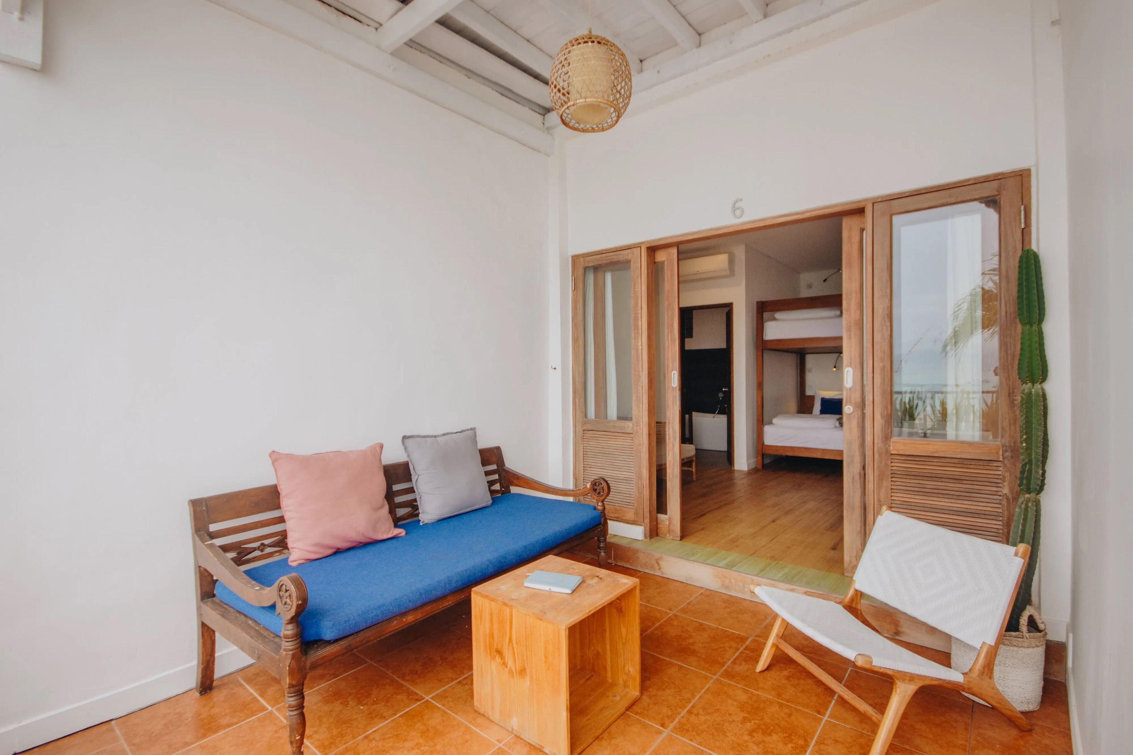 Ein Zimmer mit einer Holzsofa, einem kleinen Holztisch, einem weißen Stuhl und einer großen Sukkulente.