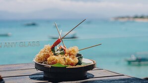 Un plato de mariscos sobre una mesa de madera, con vista al mar y barcos al fondo.