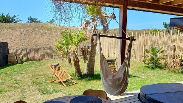Une terrasse en bois avec une table ronde et des chaises, un fauteuil suspendu et un hamac.