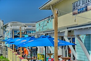 Outdoor seating with blue umbrellas, a building with a 'Half Hitch' sign, and a view of a bridge in the background.