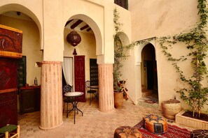 Un patio interior con arcos, un farol colgante, una puerta roja y una planta en maceta.