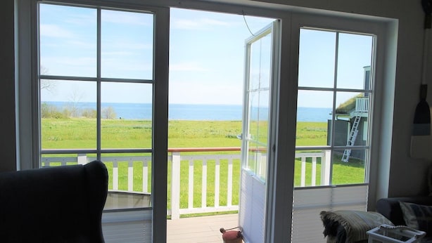 Una habitación con un gran ventanal corredero que da a un balcón con vistas al océano y a una zona verde.