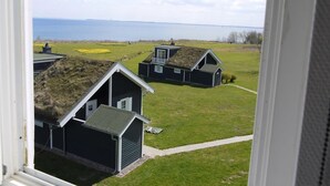 Vista de casas tradicionales con techos de hierba, un campo cubierto de césped y una masa de agua al fondo.