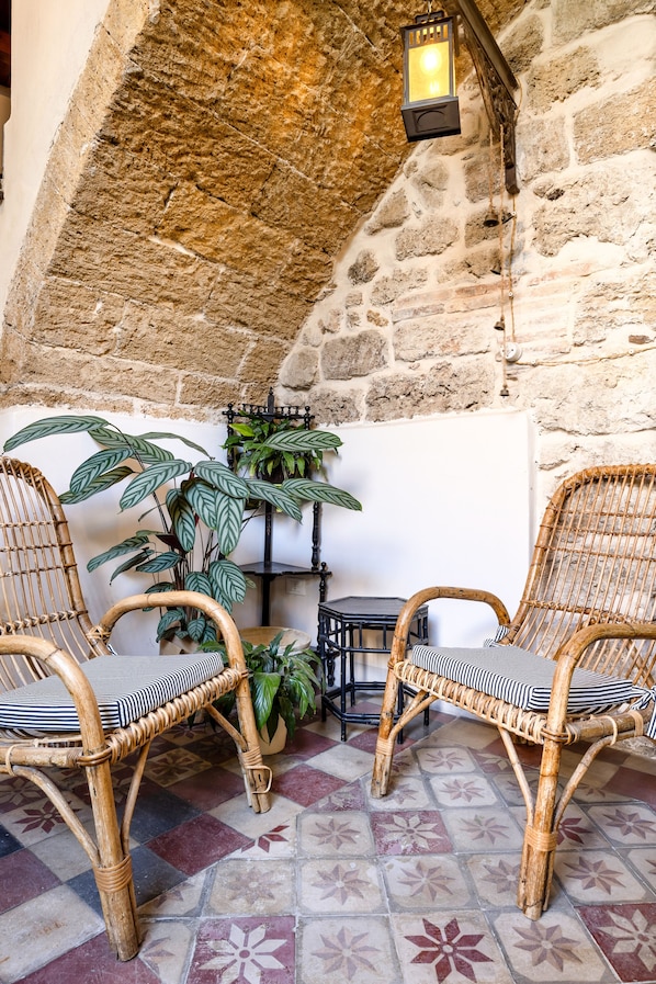 A cozy seating area with wicker chairs and a potted plant, set against a stone wall with a hanging lantern. - Locanda sette fate SPA e Solarium (Palermo)