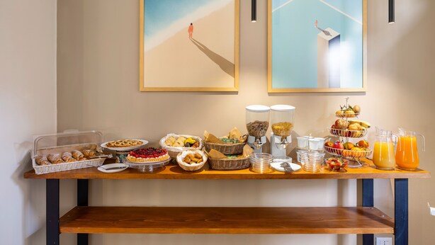 Un bufé de desayuno con diversas opciones de comida y bebidas, una obra de arte enmarcada en la pared y una mesa de madera.