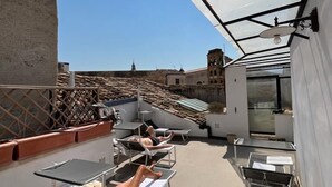 Terraza en la azotea con tumbonas y un cerramiento de vidrio, con vistas a la ciudad.