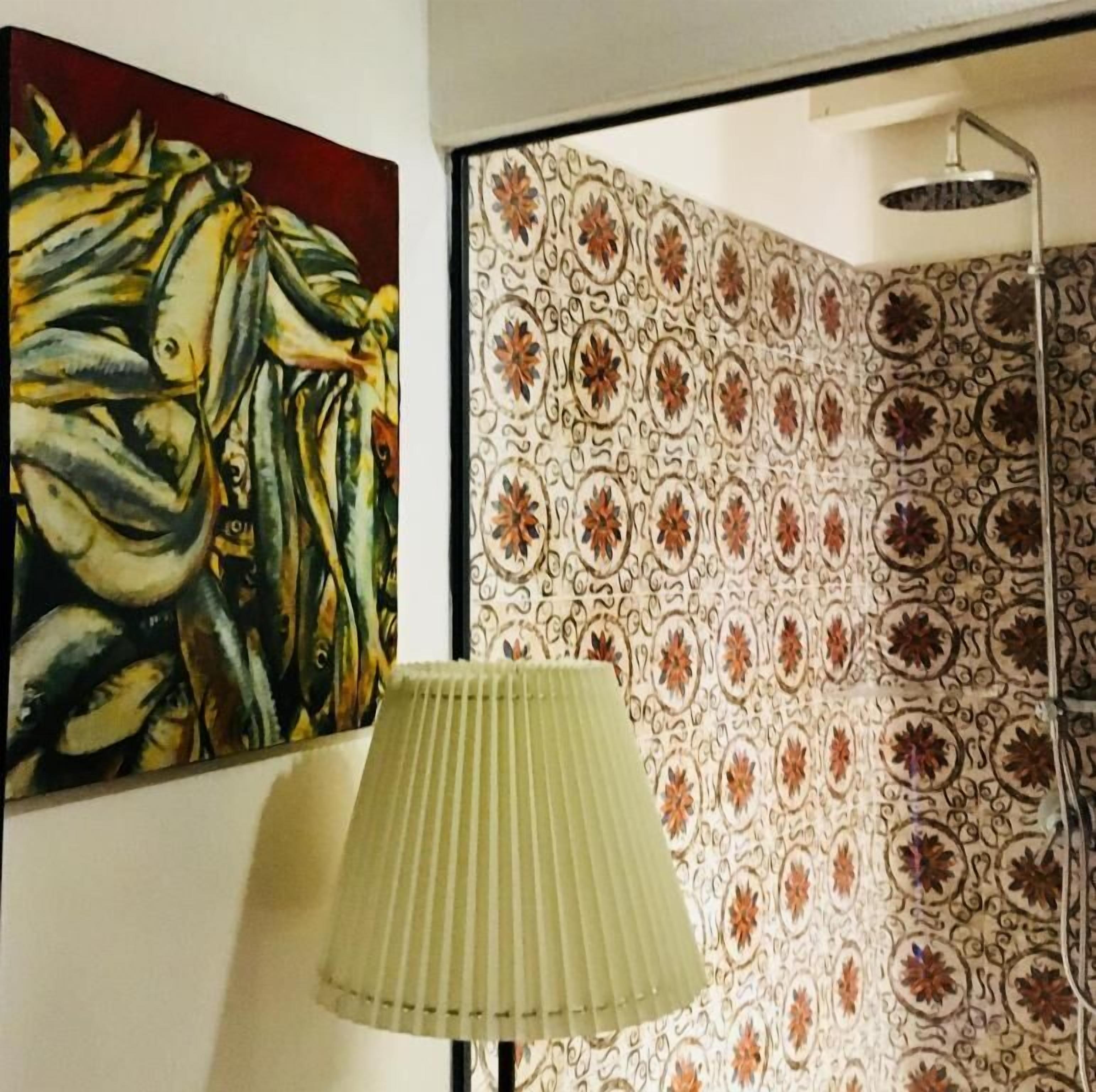 Une pièce avec un papier peint à motifs, un tableau représentant des poissons et un lampadaire.
