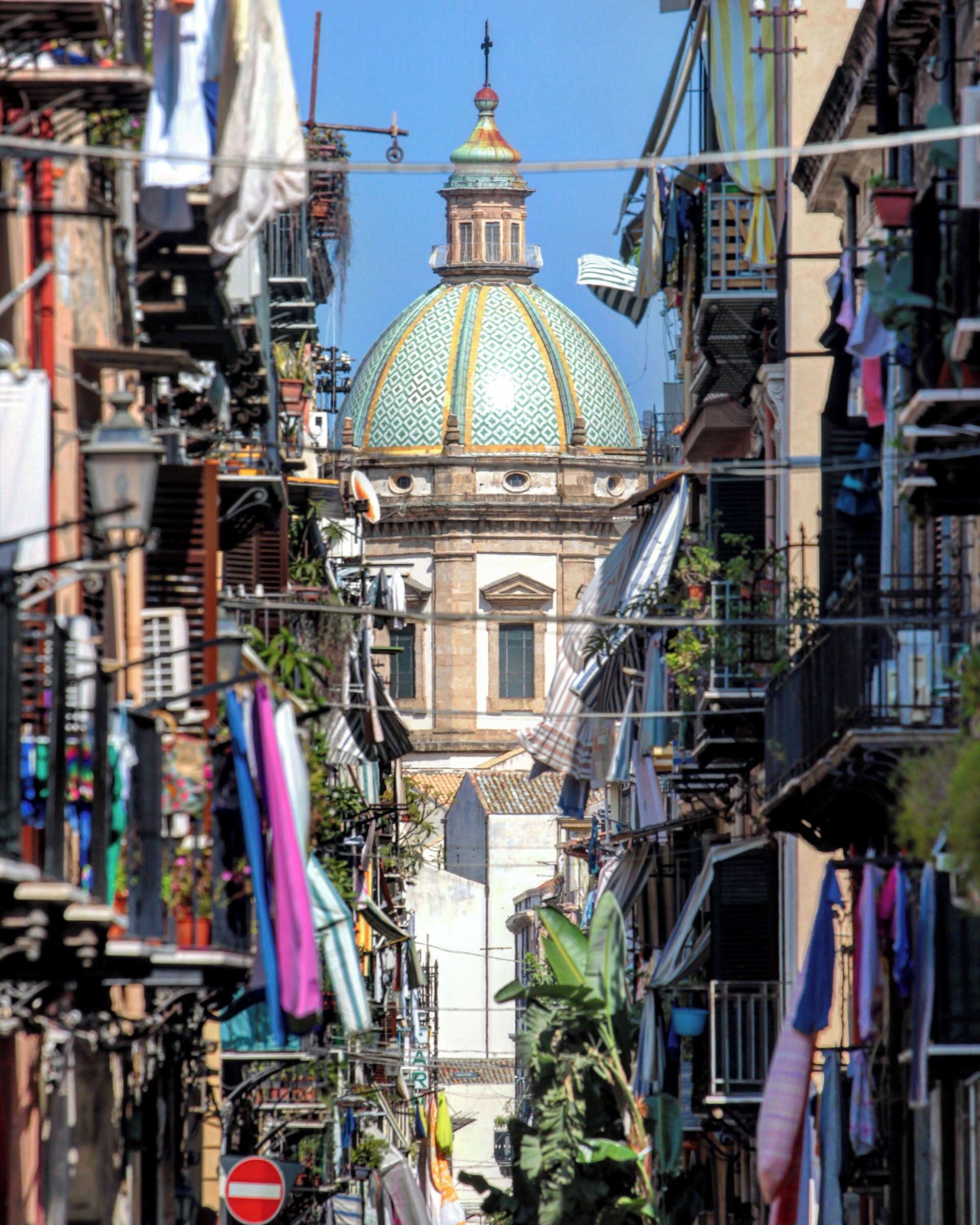 A narrow street with a prominent building featuring a large dome and a clock tower.