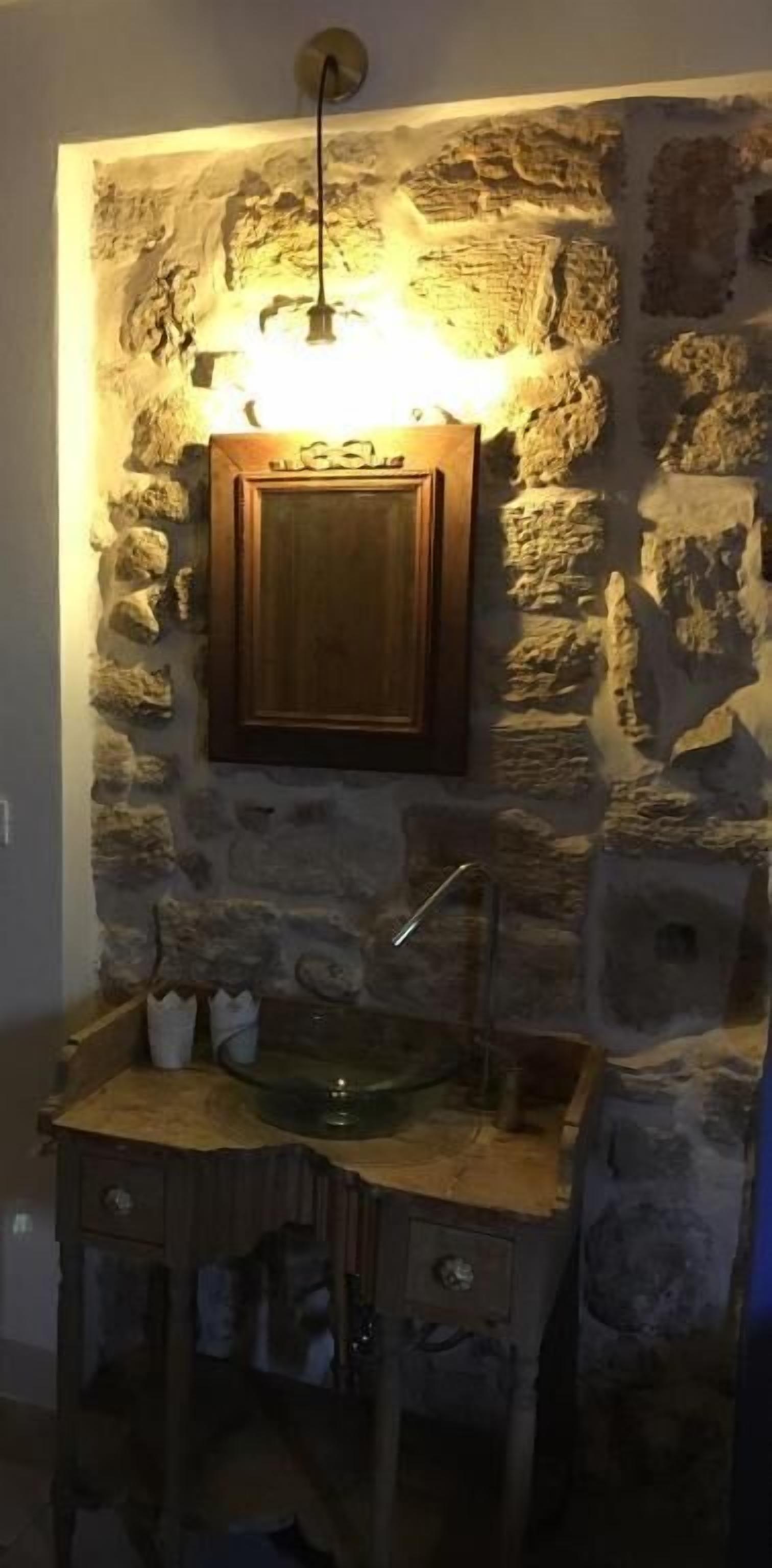 A bathroom with a stone wall, a wooden cabinet, and a sink.