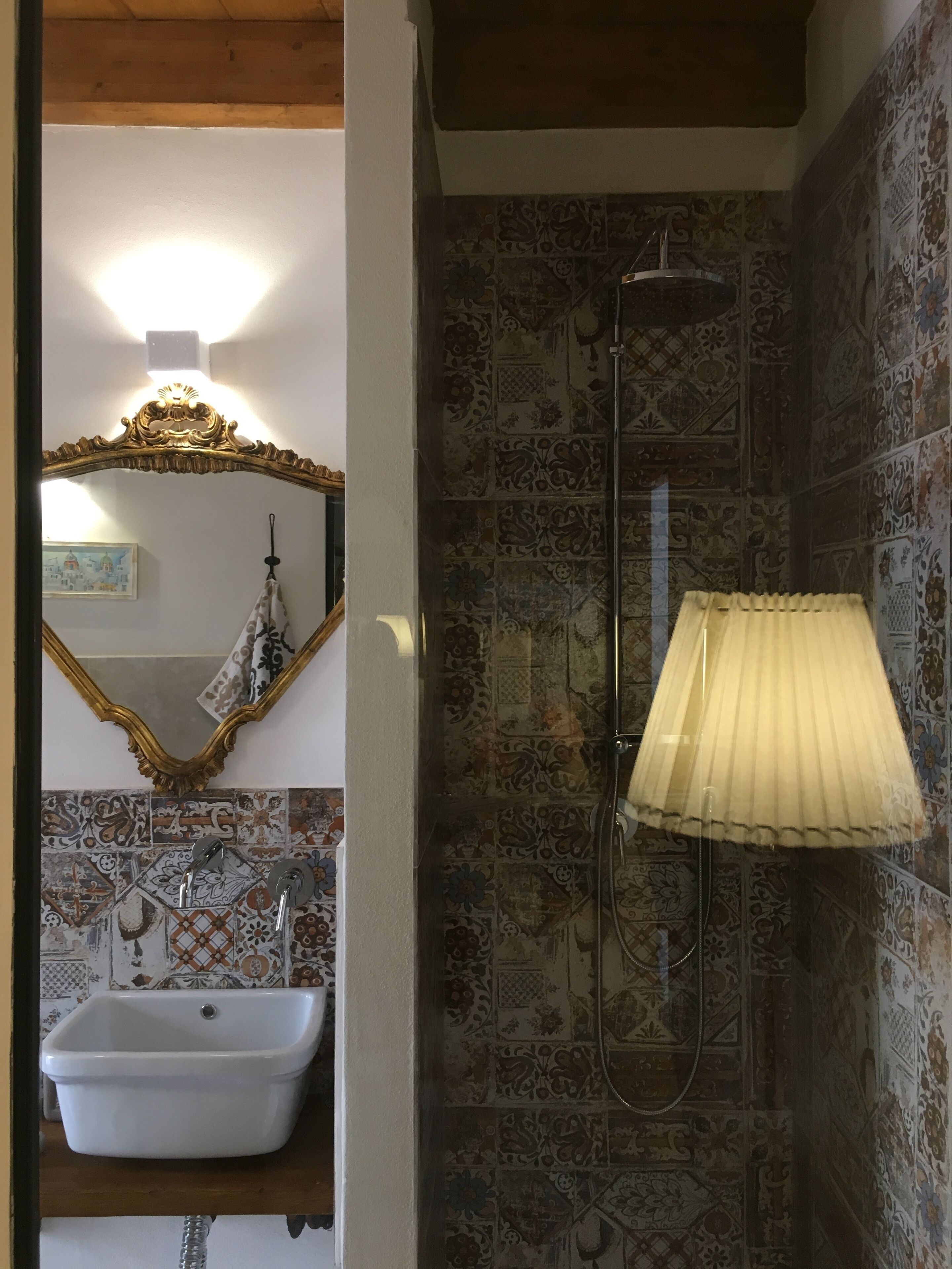 Un baño con un lavamanos blanco, un espejo con un marco decorativo y una ducha con una toalla color beige.