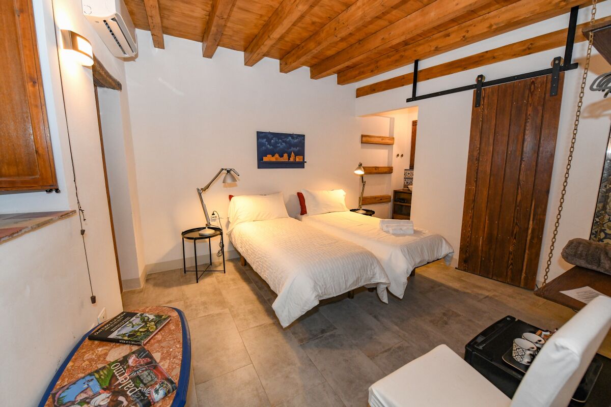A cozy bedroom with a double bed, bedside tables, a small desk with a chair, and a wooden ceiling.