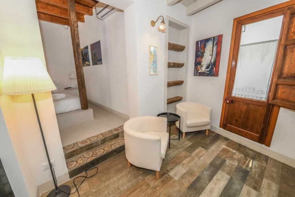 A modern interior with a wooden door, white walls, and a patterned floor. There are two white armchairs and a small table.