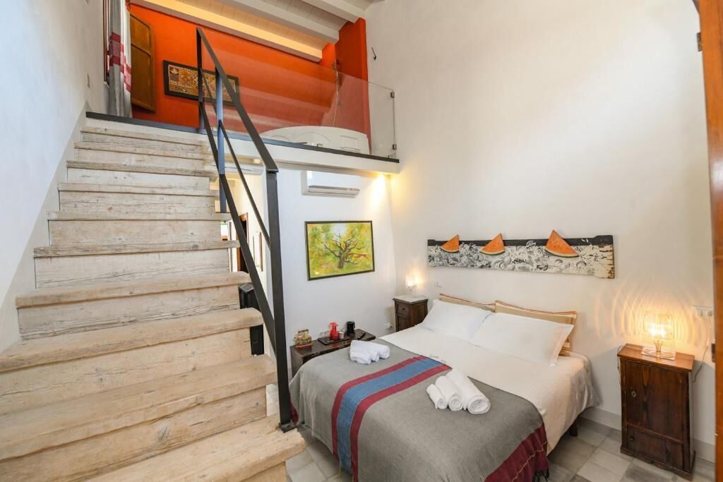 A bedroom with a bed, a nightstand, a lamp, a painting, and a staircase.