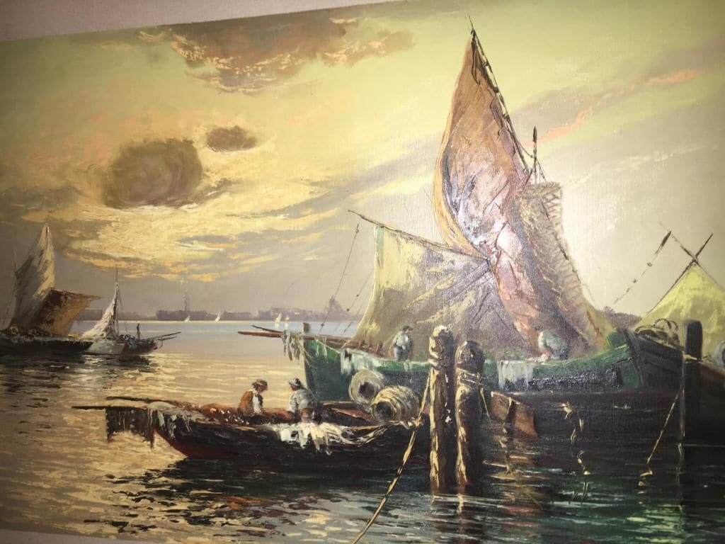 A large painting of a harbor scene with multiple boats and a sunset.