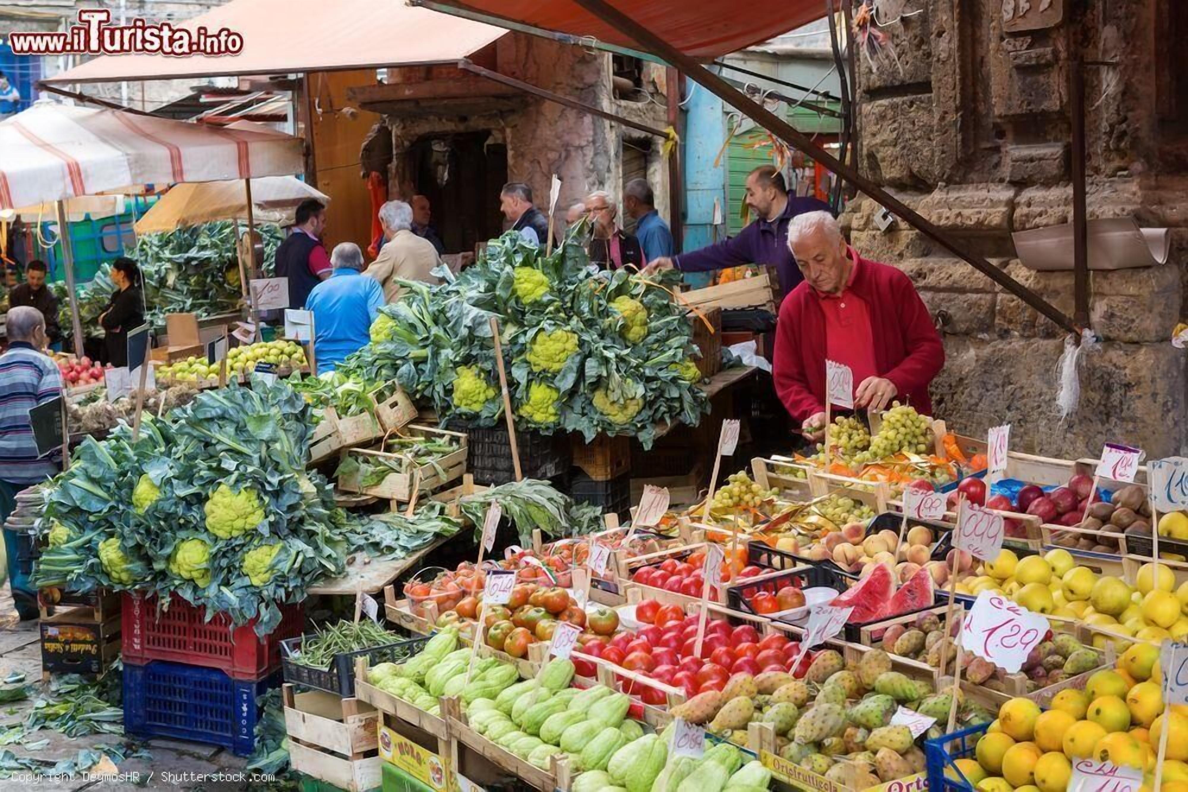 A bustling outdoor market with various fresh produce displayed on wooden crates and tables.