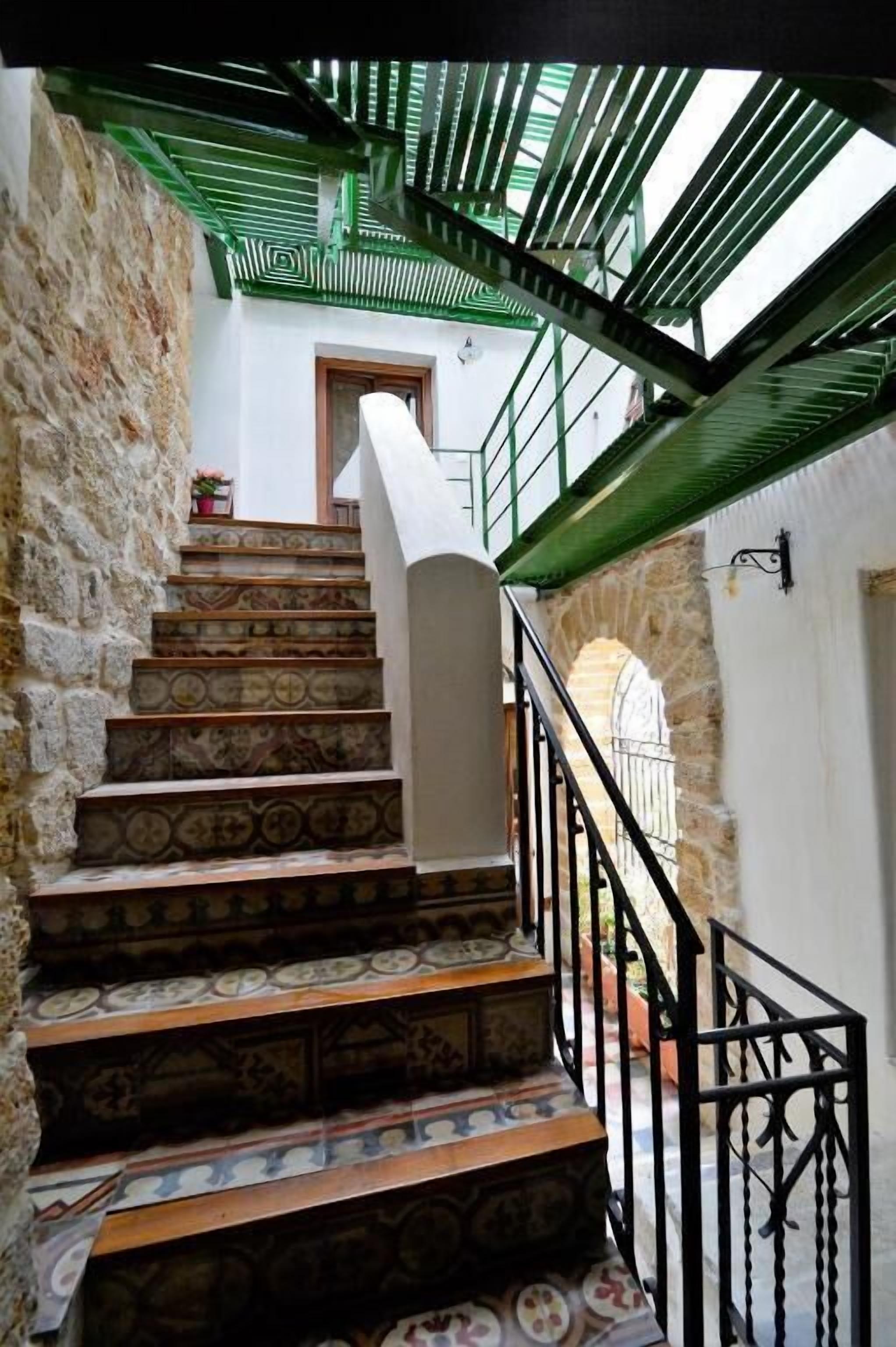 Una escalera con baldosas estampadas, un muro de piedra y una barandilla de metal verde.