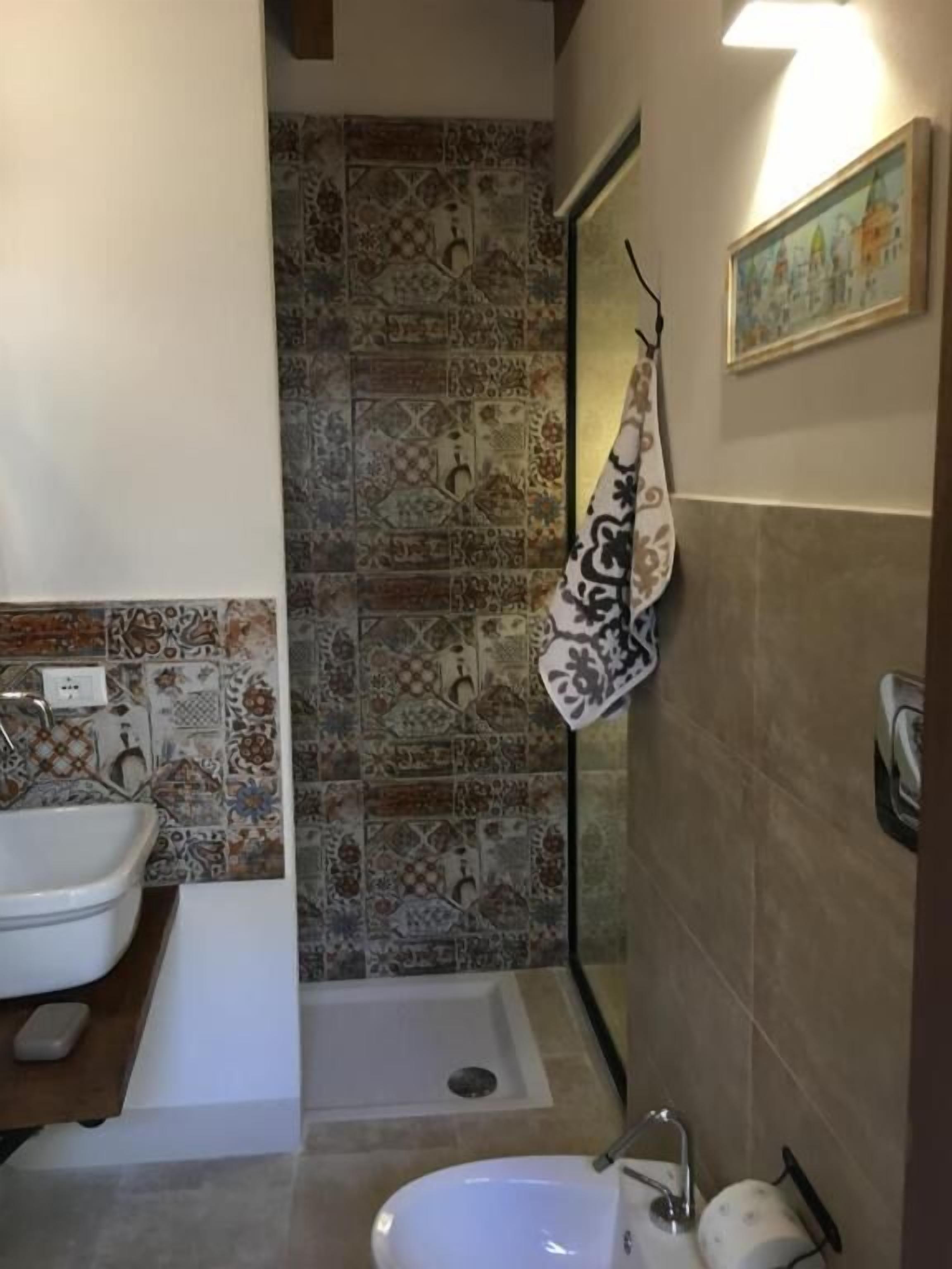 Un baño con lavamanos blanco, bañera y zona de ducha. Las paredes están revestidas con un diseño estampado.
