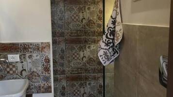 Un baño con lavamanos blanco, bañera y zona de ducha. Las paredes están revestidas con un diseño estampado.