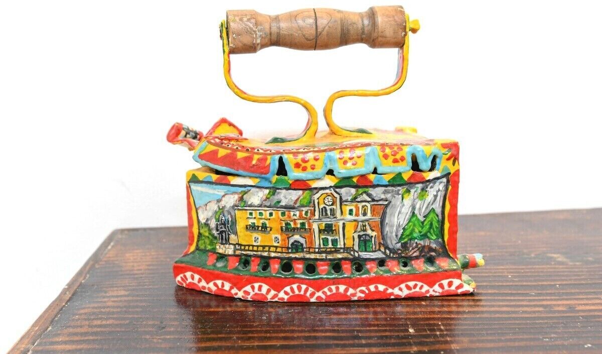 A colorful, hand-painted metal kettle with a wooden handle and a detailed illustration of a building on its body.
