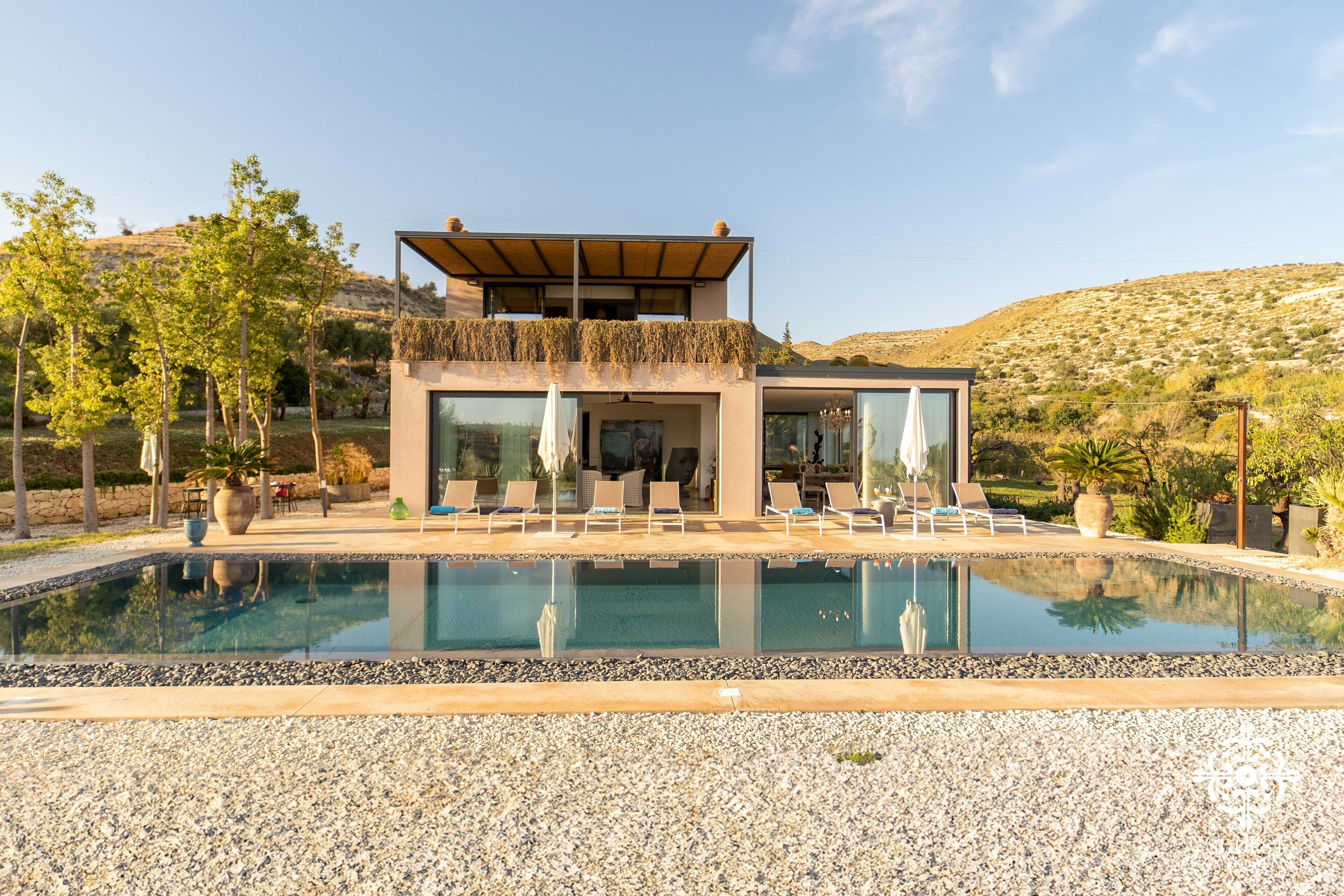 A modern house with a pool, outdoor seating, and a view of the surrounding landscape.