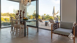 A dining area with a table and chairs, a chandelier, and a view of the outdoors. - Villa Dama - Luxury Escape (Avola)