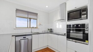 A modern kitchen with white cabinets, stainless steel appliances, and a window providing natural light. - Elliston Esplanade Beach House (RUFF-INN-IT) (Elliston)