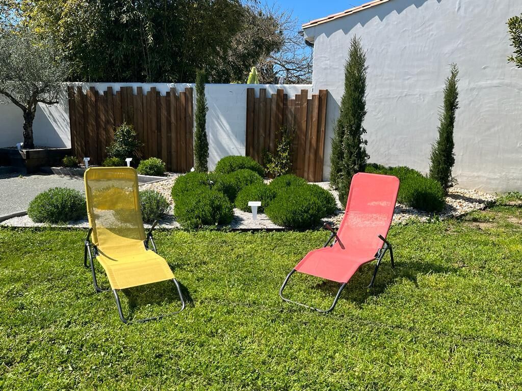 Two outdoor chairs in a well-maintained garden area with a white wall and wooden fence in the background.