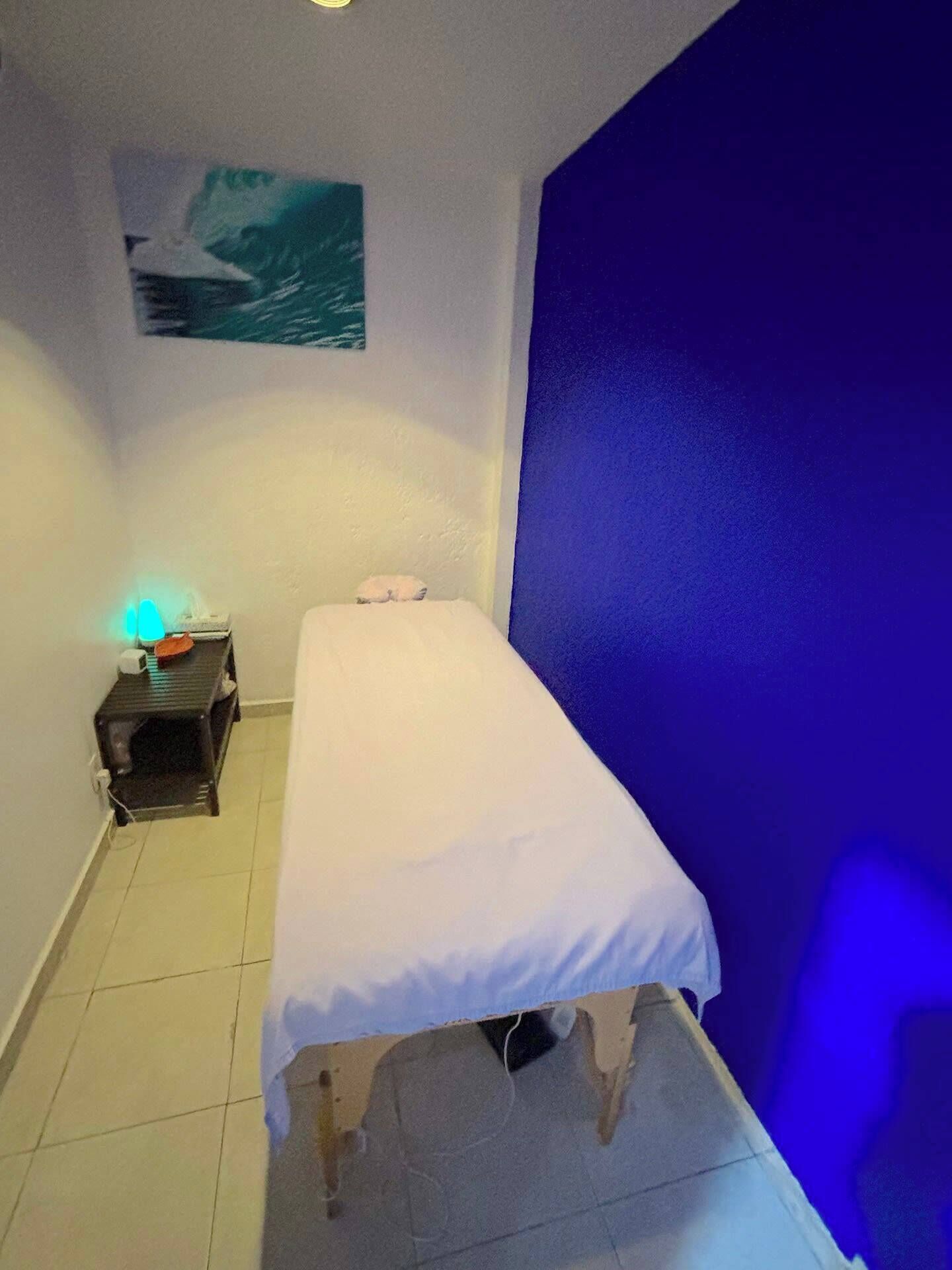 Ein kleiner, privater Raum mit einem Einzelbett, einem Nachttisch mit Lampe und einer Wand mit einem Gemälde.