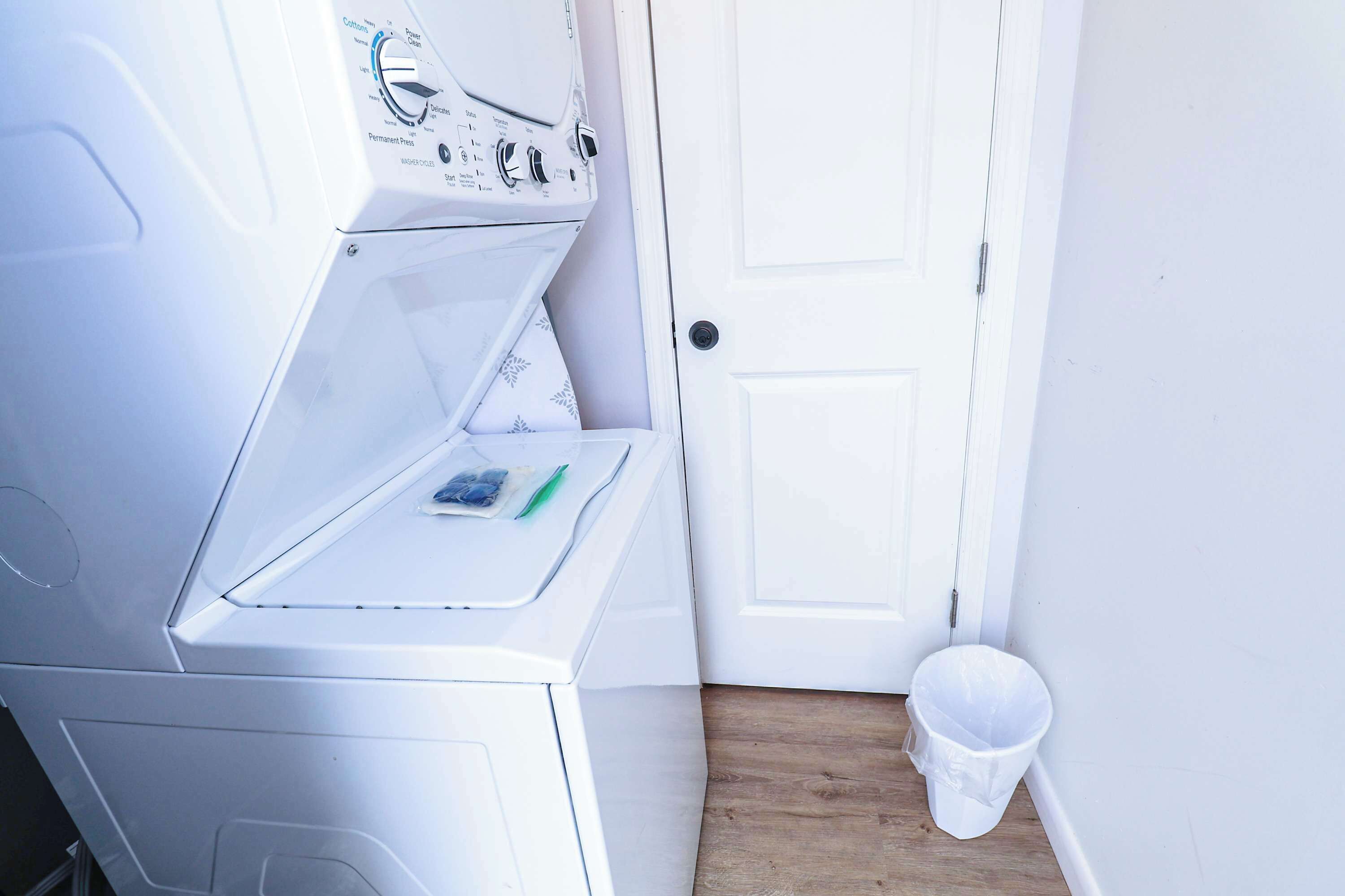 A compact laundry room with a washing machine, a dryer, and a small trash bin.