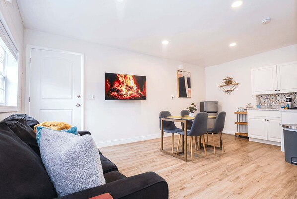 Una sala moderna con un sofá, una mesa de comedor con sillas, un televisor y una zona de cocina con armarios y encimera.