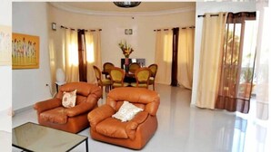 A living room with two leather armchairs, a glass coffee table, and a dining area with a table and chairs. - Chez Ouly (Dakar)