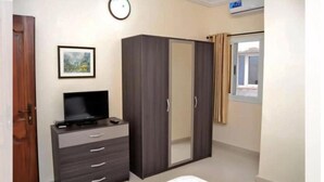 A bedroom with a wardrobe, a television on a dresser, a framed picture on the wall, and a window with curtains. - Chez Ouly (Dakar)