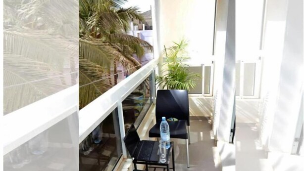 A balcony with a glass railing, a laptop, two chairs, a water bottle, and a potted plant. - Chez Ouly (Dakar)