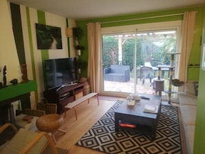 Ein Wohnzimmer mit Fernseher, Sofa, Couchtisch und Blick ins Freie.