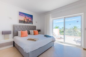 A bedroom with a large bed, a nightstand, a painting, and a sliding glass door leading to a balcony. - Casa Rosa at Boavista Resort (Lagos)