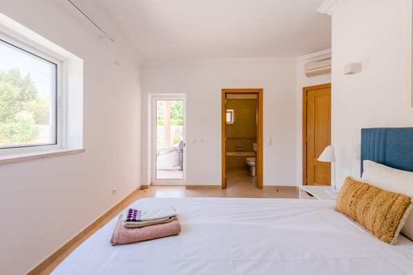 A bedroom with a large bed, a window, and a bathroom visible through an open door. - Casa Rosa at Boavista Resort (Lagos)