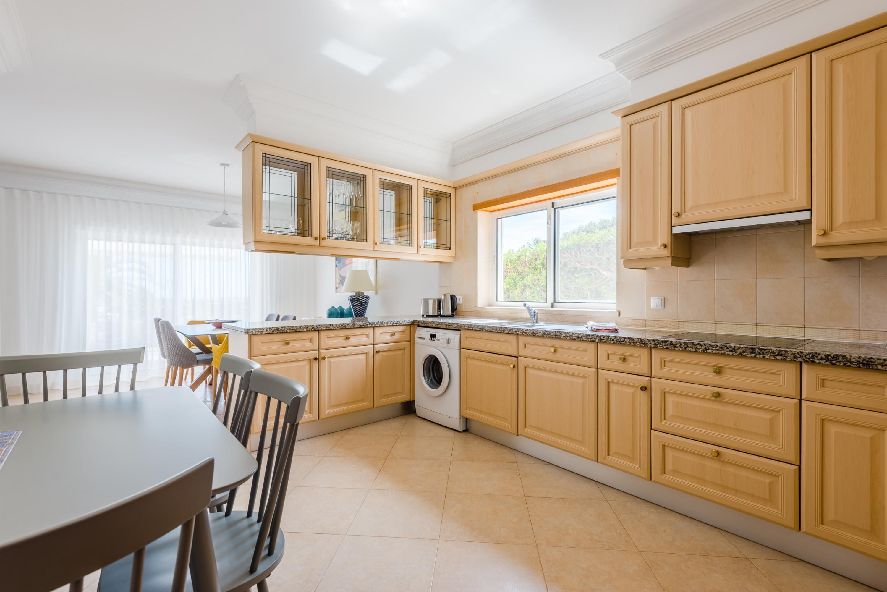 A modern kitchen with wooden cabinets, a built-in washing machine, and a dining area with a table and chairs.