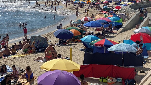 Une plage bondée, avec de nombreux parasols colorés, où les gens profitent du beau temps.