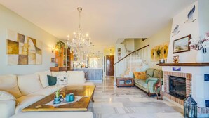 Un vaste salon doté d’une cheminée, d’un lustre et d’un escalier menant à un niveau supérieur.