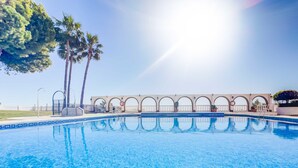 Une piscine d’un bleu éclatant, bordée de carreaux, entourée d’une clôture blanche et de palmiers.
