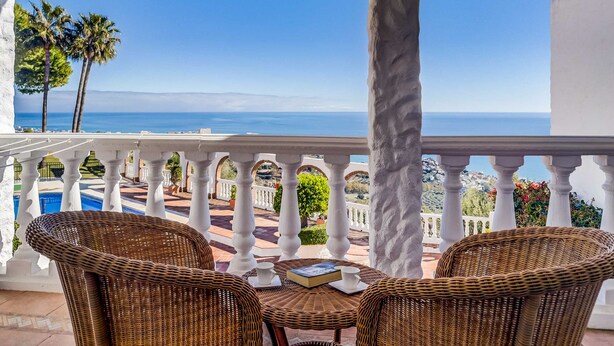 Un balcon avec des meubles en osier, une vue sur la mer et des palmiers.