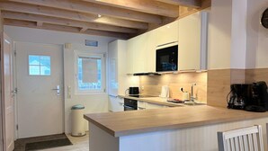 Una cocina moderna con vigas de madera, microondas integrado, cafetera y un ventanal pequeño.