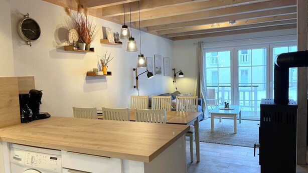 Una cocina moderna con lavadora integrada, vigas de madera en el techo, luces colgantes y vistas al balcón exterior.