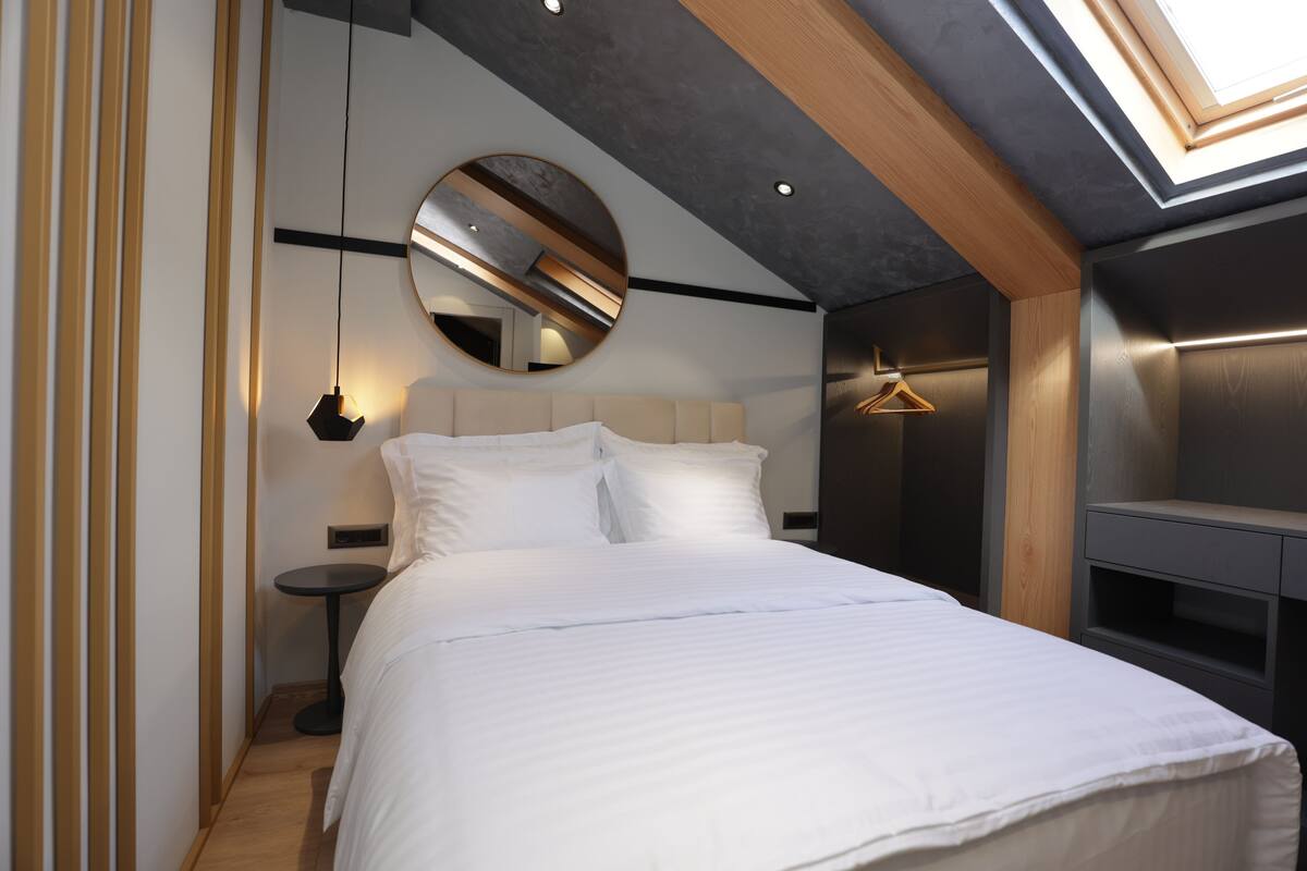 A modern bedroom with a large bed, a round mirror, a bedside table, and a hanging light fixture.