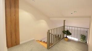 Un intérieur moderne avec une porte en bois, un escalier doté d’une rampe et une plante en pot sur le palier.