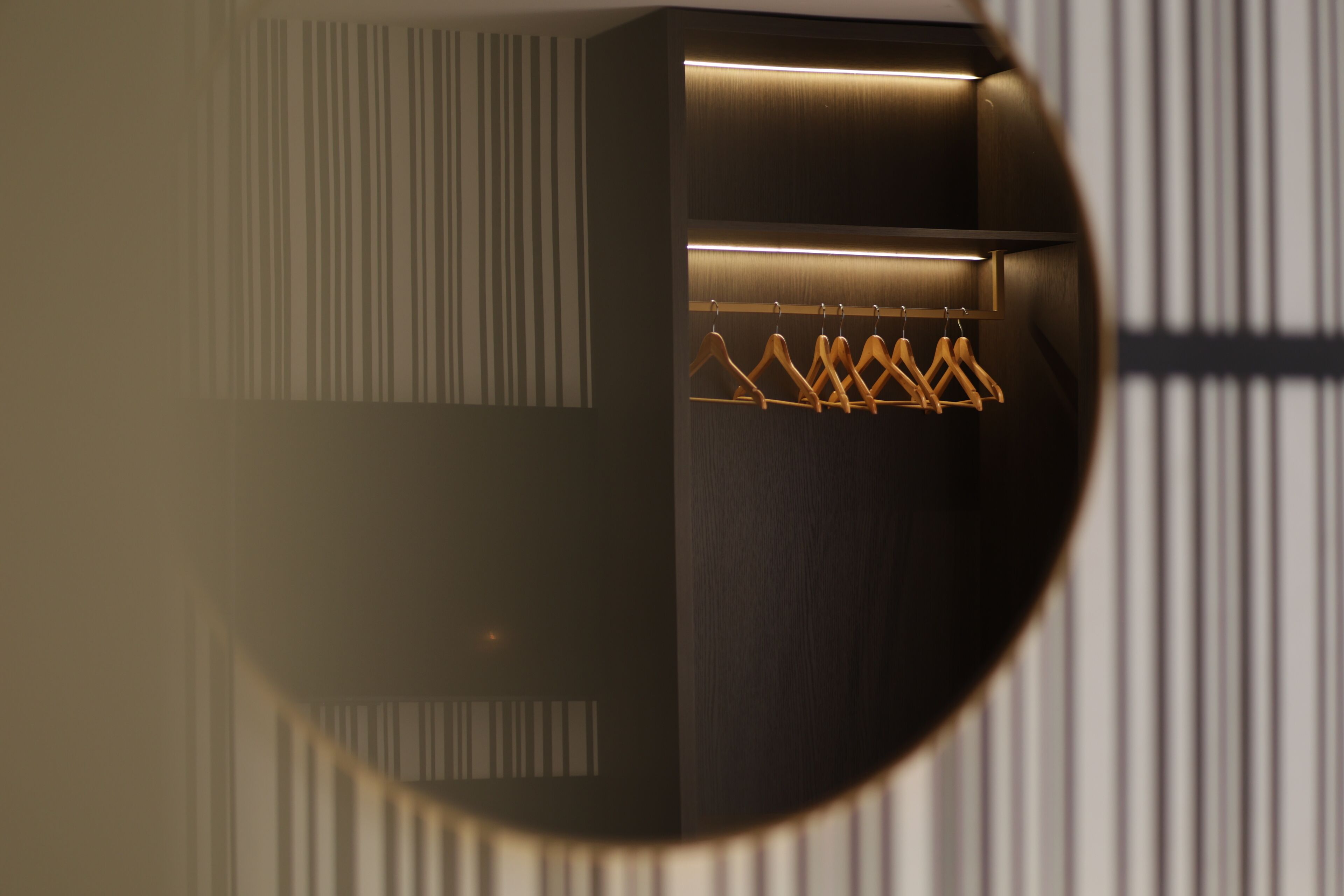 A circular view of a room with a wooden wardrobe, a hanging rack with clothes, and a striped wall pattern.