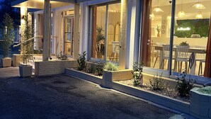 Een modern huis met grote glazen deuren, een overdekte veranda en een goed verlicht interieur, zichtbaar door de ramen.