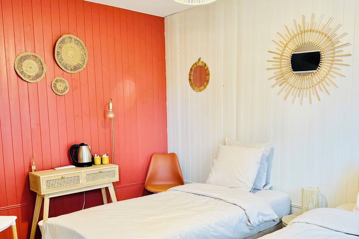 Une chambre avec deux lits, un bureau, une chaise et un luminaire suspendu.