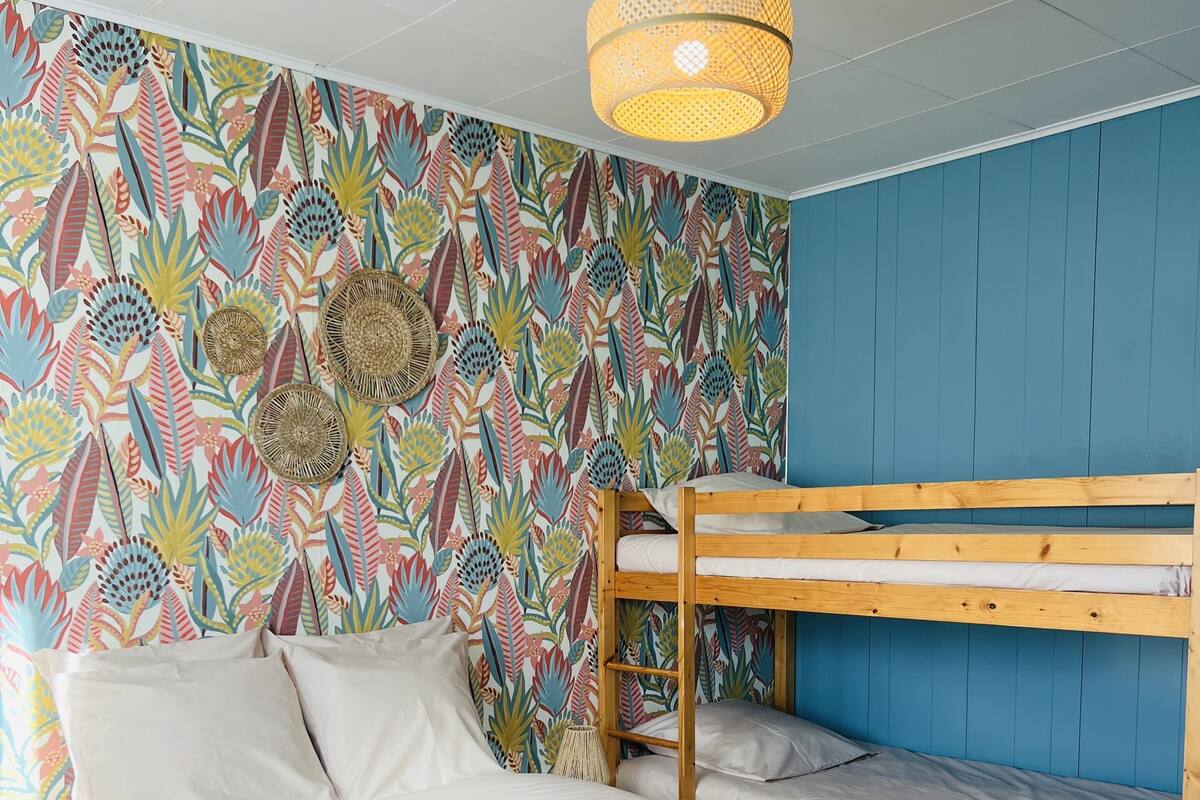 Une chambre avec un lit superposé, un lit simple, un mur à motifs, un luminaire suspendu et un tapis tissé.