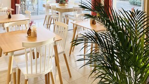 Een restaurant met ronde tafels, witte stoelen en hangende rieten lampen.